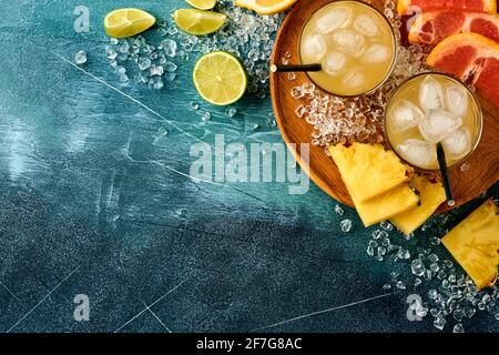 Jus d'ananas frais avec glace et variété tranchés mûrs de couleur fruits tropicaux pamplemousse, orange, citron vert, composition de la couche plate, sur le bleu foncé st Banque D'Images