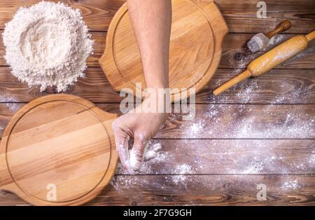 La main du chef saupoudrer la farine de blé sur des planches à pizza rondes en bois, des œufs de poulet et une broche roulante sur fond de plateau brun. Mise au point sélective. Prép Banque D'Images