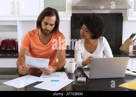 Divers couples assis dans la cuisine avec un ordinateur portable et payer des factures Banque D'Images