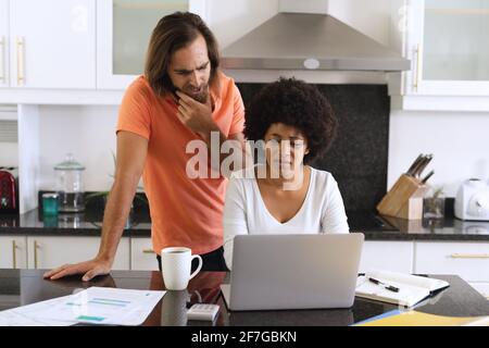 Divers couples assis dans la cuisine avec un ordinateur portable et payer des factures Banque D'Images