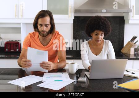 Divers couples assis dans la cuisine avec un ordinateur portable et payer des factures Banque D'Images