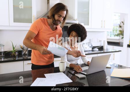 Divers couples assis dans la cuisine avec un ordinateur portable et payer des factures Banque D'Images