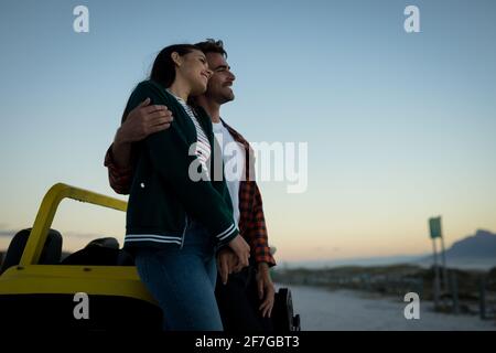 Heureux couple caucasien se penchant contre la promenade de plage au bord de la mer au coucher du soleil Banque D'Images