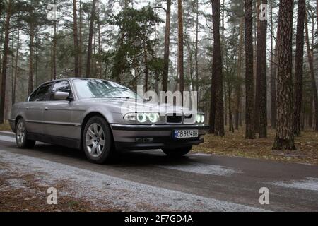 Chernigov, Ukraine - 6 janvier 2021: Ancienne voiture BMW série 7 (E38) sur la route dans la forêt. Temps sombre Banque D'Images