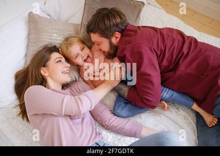 La famille joue avec l'enfant sur le lit. Mère et père rient avec la petite fille. Banque D'Images