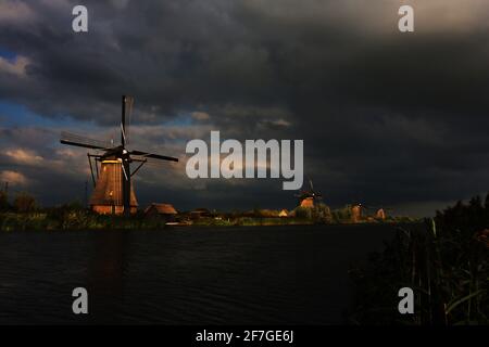 romantische Windmühle am Rande eines Kanals in Kinderdijk mit dramatischer Wolkenstimmung am frühen Abend in Holland, Niederlande Banque D'Images