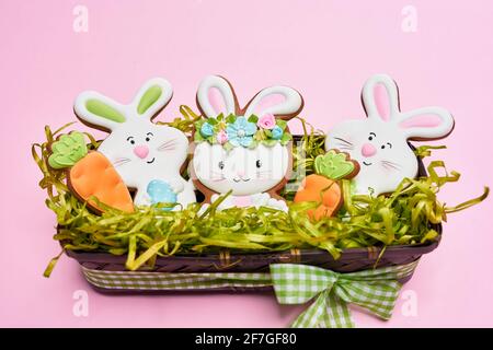 Biscuits au sucre de Pâques décorés de glaçage coloré sous forme de lapins blancs et de carottes orange. Panier en bois avec décoration de Pâques sur fond pastel. Banque D'Images