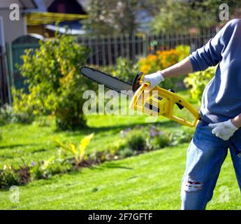 les mains des femmes avec une scie à essence jaune en plein air. le concept de jardinage et de construction dans le jardin et le potager. Banque D'Images