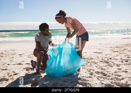 Un couple afro-américain heureux portant des gants en latex pour ramasser les déchets la plage Banque D'Images