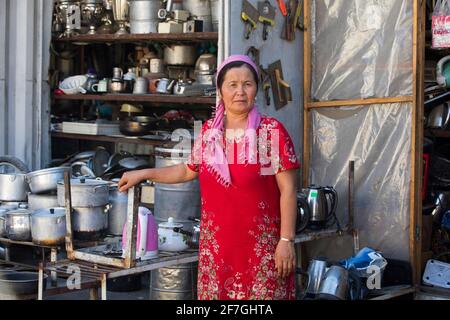 Femme kirghize avec un foulard vendant des ustensiles de cuisine, des casseroles et des poêles sur le marché dans la ville d'Osh, Kirghizistan Banque D'Images