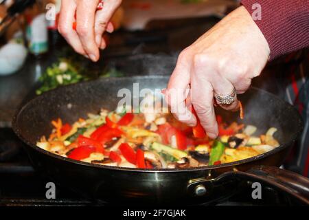 Gros plan des mains d'une femme ajoutant du poivre rouge à un poêlon dans une poêle. Banque D'Images