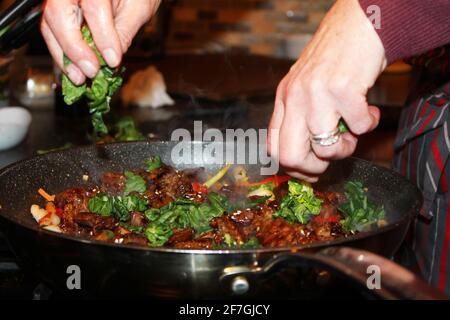 Gros plan des mains de la femme ajoutant Bok choy à un sauté de bœuf coréen, Bulgogi Banque D'Images