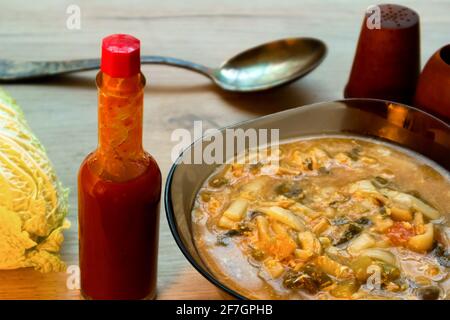 Soupe de nouilles asiatiques épicée dans un bol en verre, sauce tabasco et chou chinois servis sur une planche de bois Banque D'Images