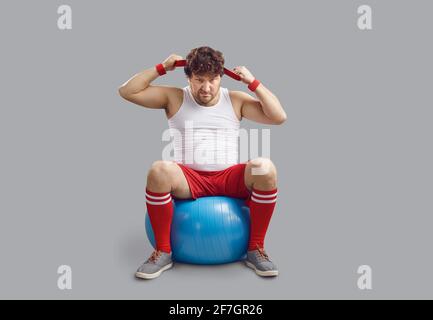 Drôle d'homme de chubby en colère assis sur le ballon de fitness et obtenir prêt pour l'entraînement de gym Banque D'Images