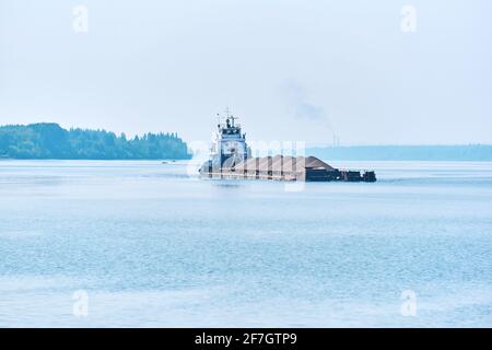 le remorqueur pousse la barge de cargaison en vrac sèche avec du sable sur le rivière dans la brume matinale Banque D'Images