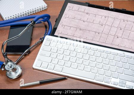 Table du cardiologue avec tablette PC et électrocardiogramme. Stéthoscope et stylo. Concept de santé et de médecine. Banque D'Images