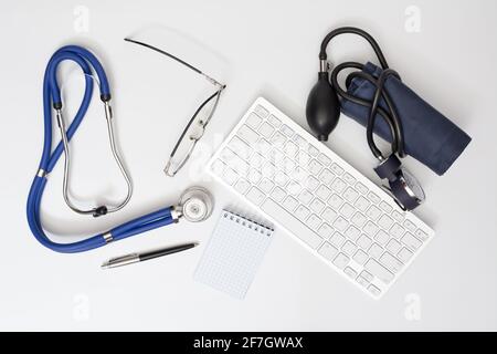 Stéthoscope et tonomètre sur la table du cabinet du médecin. Vue de dessus de la table de bureau avec clavier d'ordinateur sans fil, lunettes et ordinateur portable avec stylet. Banque D'Images