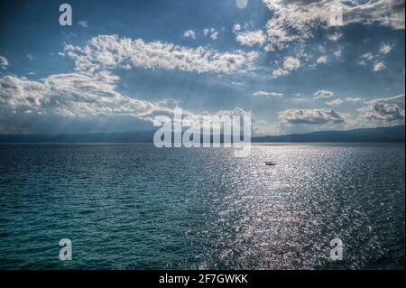 Bateau dans l'eau du lac, montagnes au loin, nuages épais dans le ciel. Bleu et vert avec beaucoup de détails. Banque D'Images
