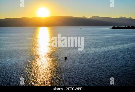 Les couleurs du soleil couchant se reflètent dans l'eau.bateau dans l'eau du lac, montagnes au loin, nuages épais dans le ciel. Coucher de soleil jaune. Banque D'Images