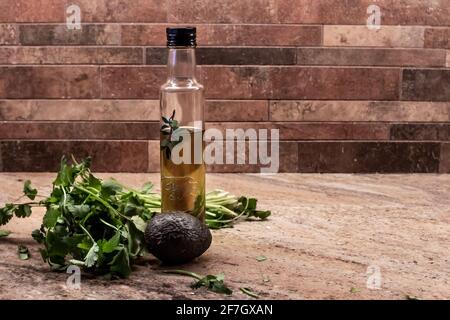 Une bouteille d'huile d'olive naturelle maison parmi les feuilles de coriandre et un petit avocat mûr sur un comptoir en marbre en Ontario, Canada. Banque D'Images