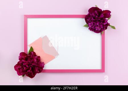Cadre rectangulaire rose avec centre blanc, pivoines sur les côtés, petite enveloppe avec carte sur fond rose pastel, espace de copie. Pose à plat, style minimaliste Banque D'Images
