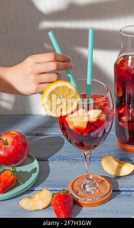 Vue sur un verre de sangria avec pailles et un prendre l'un d'eux à la main pour boire la sangria avec une assiette de fruits et une bouteille de sangria sur un soleil Banque D'Images