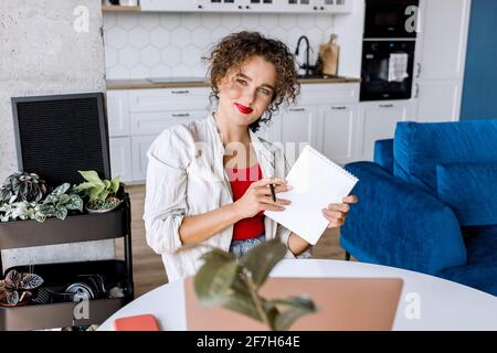 Portrait d'une femme d'affaires confiante et élégante prend des notes, regarde l'appareil photo, sourit. Jeune femme indépendante ou étudiante réussie à distance Banque D'Images