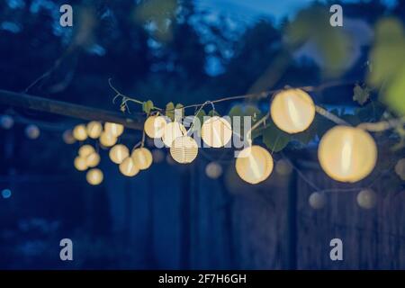 Rangée de lanternes rondes en papier dans un jardin sur un fond de chaume en bois la nuit. Décoration festive dans le jardin le soir. Banque D'Images