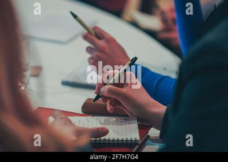 Détails de personnes inconnues écrivant des notes, tenant des stylos et utilisant un carnet pour des croquis et des détails sur une réunion d'affaires ou un congrès. Banque D'Images