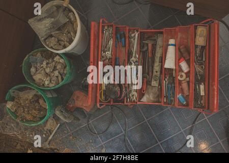 Flatlay photo de boîte à outils ouverte rouge assis sur le sol d'un chantier de construction dans un appartement. La boîte à outils contient des outils, des tournevis, des pinces et une clé Banque D'Images