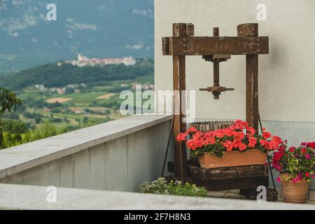 Une vieille presse à raisin pour faire du vin est debout sur un balcon avec une belle vue sur un vieux village sur la colline en arrière-plan. Banque D'Images