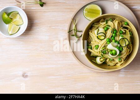 Bol de pâtes linguine avec sauce à l'avocat, petits pois verts, courgettes, pousses sur table rustique en bois blanc, vue sur le dessus Banque D'Images