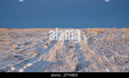 Route de campagne dans un champ enneigé contre un ciel bleu à l'heure d'or. Concept de voyage local. Banque D'Images