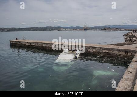 Un petit bateau en plastique a partiellement coulé sous l'eau dans une petite marina près d'un port de Koper en Slovénie. Des débris ou des déchets sont visibles dans l'eau. Banque D'Images