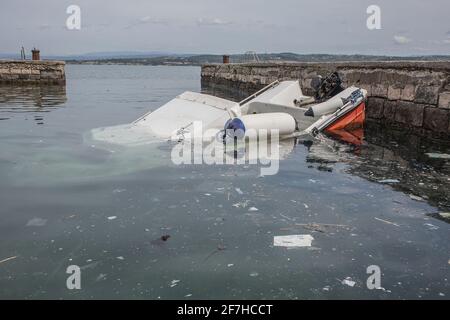 Un petit bateau en plastique a partiellement coulé sous l'eau dans une petite marina près d'un port de Koper en Slovénie. Des débris ou des déchets sont visibles dans l'eau. Banque D'Images