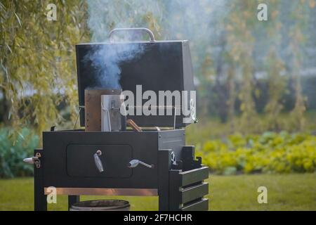 Le grill fumeur dans une cour intérieure est en train d'être mis au feu. Récipient avec du bois et du charbon sur un gril prêt à être inséré dans le four. Banque D'Images