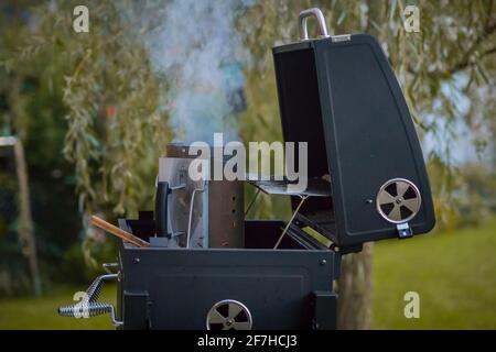 Le grill fumeur dans une cour intérieure est en train d'être mis au feu. Récipient avec du bois et du charbon sur un gril prêt à être inséré dans le four. Banque D'Images