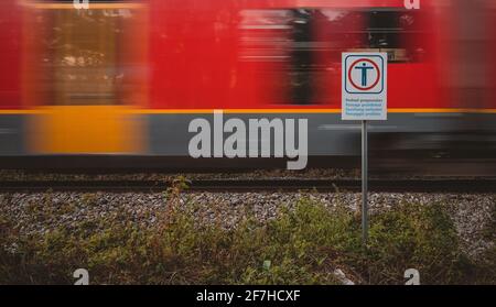 Panneau d'avertissement pour ne pas traverser la voie ferrée sur une voie de chemin de fer ouverte avec un train rouge visible se déplaçant rapidement derrière elle. Banque D'Images