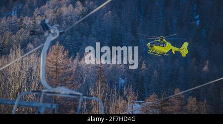 Un hélicoptère de sauvetage jaune prend au milieu de la piste de ski dans un grand nuage de neige. Concept de sauvetage en hélicoptère sur neige ou piste de ski. Banque D'Images