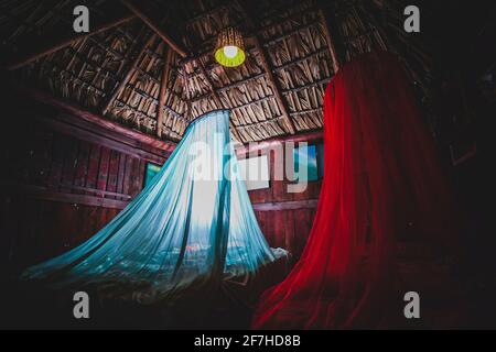 Moustiquaire blanche et rouge au-dessus du lit dans une cabane typique ou maison de campagne sur la plage à Puerto Escondido au Mexique. Le toit est fait de feuilles de palmier Banque D'Images