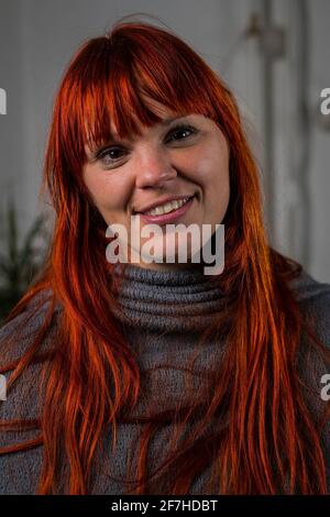 Portrait frontal d'une jeune femme à cheveux regardant l'appareil photo et portant un tapis gris ressemblant à un poncho. Emplacement à la maison dans un salon. Banque D'Images