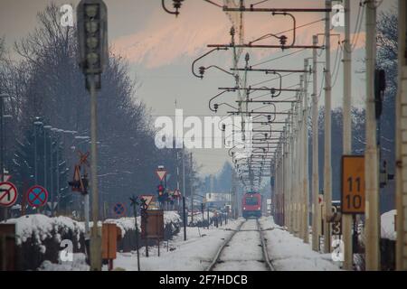 Le train rouge se dirige vers le passage à niveau, les voitures s'arrêtent juste de traverser le passage à niveau. Concept de la situation de danger de passage de chemin de fer. Banque D'Images