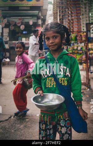 DELHI, INDE, 1er DÉCEMBRE 2016 : une fille indienne avec un chandail vert est mendiant pour de l'argent tenant un bol d'argent. Photo de concept de la pauvreté en inde pour les enfants Banque D'Images