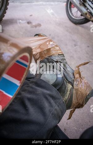 Une personne tapissant ses bottes de moto en cuir cassées ou utilisées avec du ruban brun ou du ruban de sellotape afin d'allonger leur durée de vie. Moto dans le bac Banque D'Images