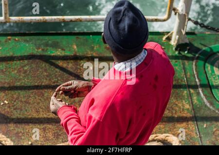 Une personne debout sur une surface de bateau verte tient une seule arachide dans ses mains et regarde vers la mer. Photo ci-dessus. Banque D'Images