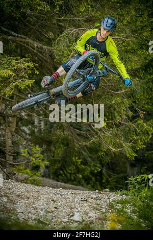 Photo frontale d'un alpiniste sautant sur un saut en terre dans un parc de vélo, entouré de forêt et d'arbres. Motard de montagne vert dans un environnement vert p Banque D'Images