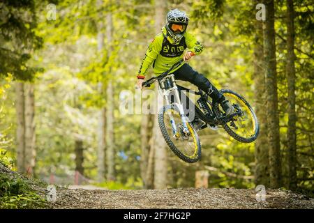 Photo frontale d'un jeune alpiniste sautant sur un saut de terre dans un parc de vélo, entouré de forêts et d'arbres. Motard de montagne dans un environnement vert Banque D'Images