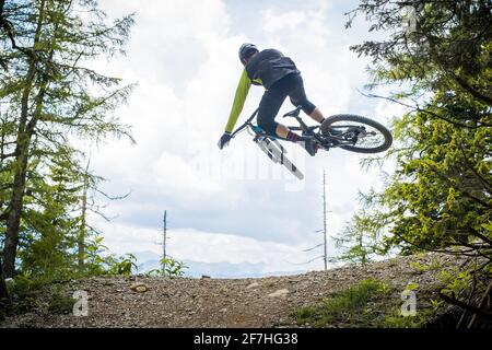 Photo arrière d'un alpiniste sautant sur un saut en terre dans un parc de vélo, entouré de forêt et d'arbres. Vélo de montagne vert dans un environnement vert avant Banque D'Images