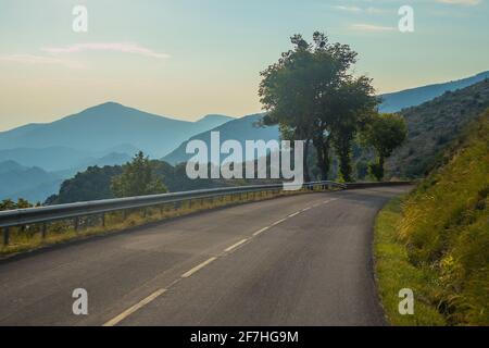 Une route sinueuse étroite dans la campagne française en début de soirée. Brume visible sur les collines en arrière-plan, les arbres sont debout sur une courbe. Bien Banque D'Images