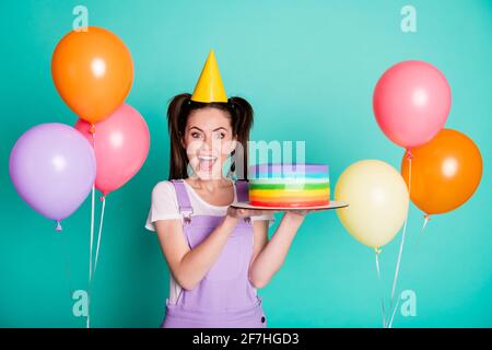 Photo de dame stupéfait tenir gâteau bouche ouverte beaucoup de ballons porter un capuchon conique en papier violet sur fond bleu sarcelle isolé Banque D'Images